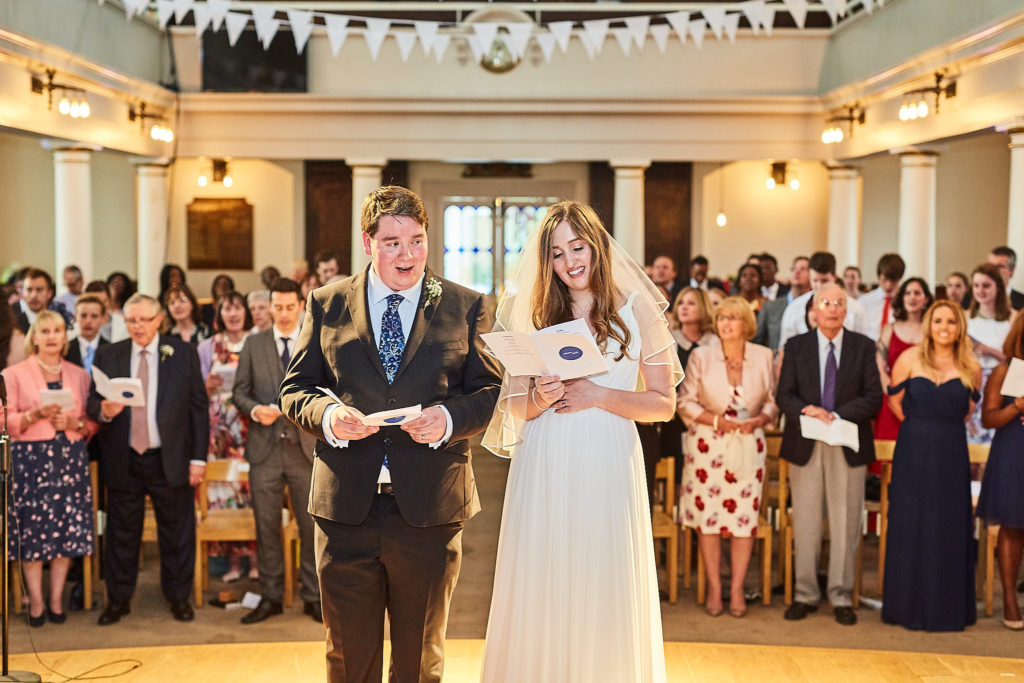 Bride and groom singing a hymn at the front of the church with the congregation behind them