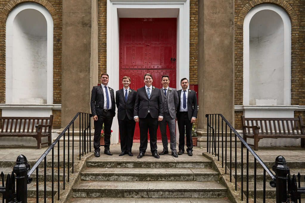 Groom and groomsmen standing on the church steps in front of the red door