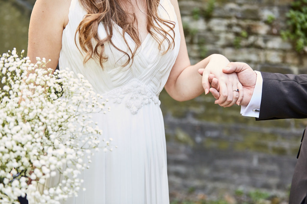 Close-up of the bride holding the groom's hand with her gypsophila bouquet
