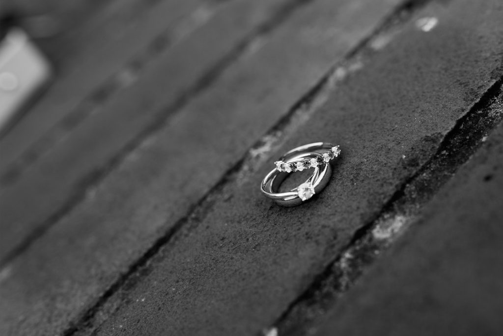 Black and white close-up of wedding rings resting on weathered wood