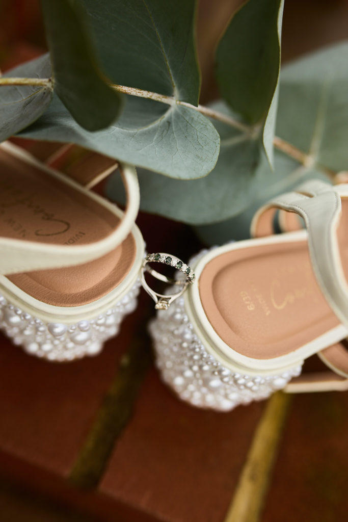 Close-up of a wedding ring resting against a pearl-studded bridal shoe heel