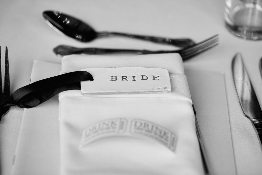 Black and white place setting with a "Bride" name card on a folded napkin