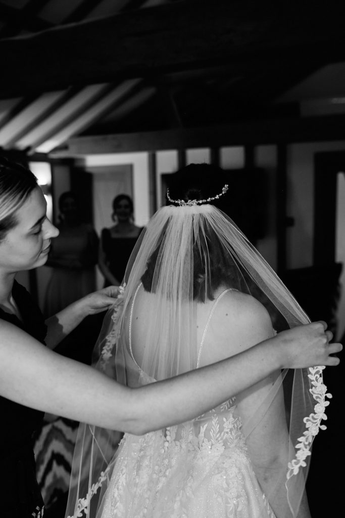 Black and white photo of the bride's veil being fitted, seen from behind