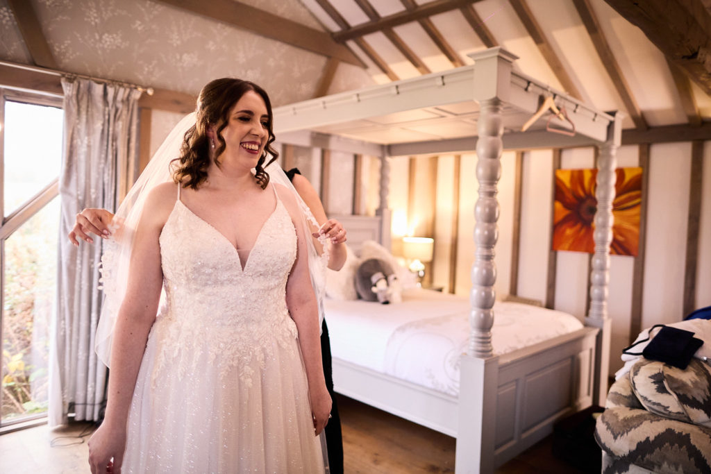 Bride laughing in her wedding dress beside a white four-poster bed