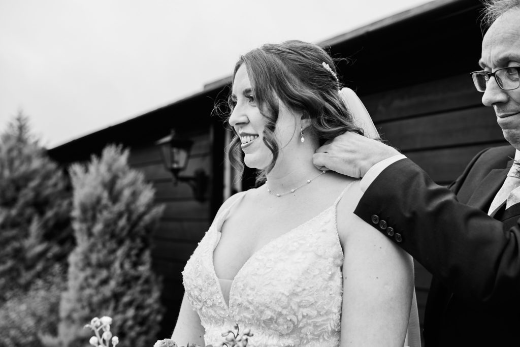 Black and white photo of the bride smiling as a man rests a hand on her shoulder