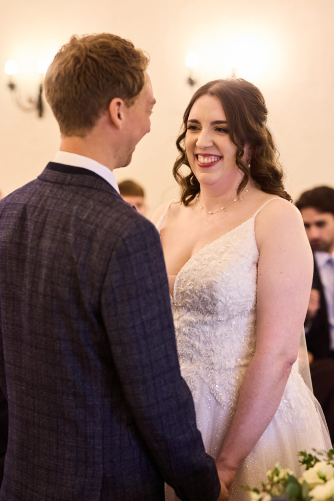 Bride smiling at the groom as they hold hands during the wedding ceremony
