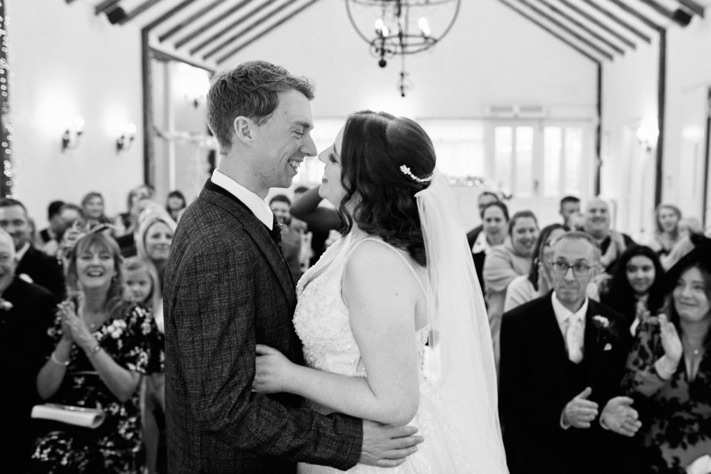 Black and white photo of the bride and groom embracing as guests applaud