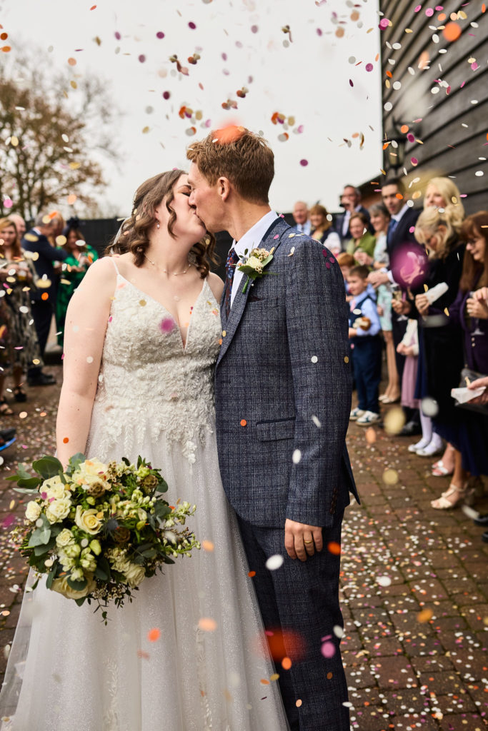 Bride and groom kissing under a shower of confetti at Crondon Park, Essex