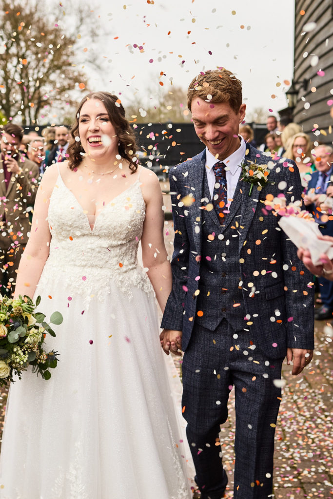 Bride and groom laughing as guests shower them with confetti at Crondon Park