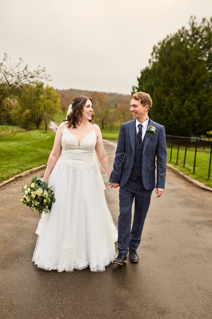 Bride and groom walking hand in hand along the driveway at Crondon Park, the bride holding her bouquet
