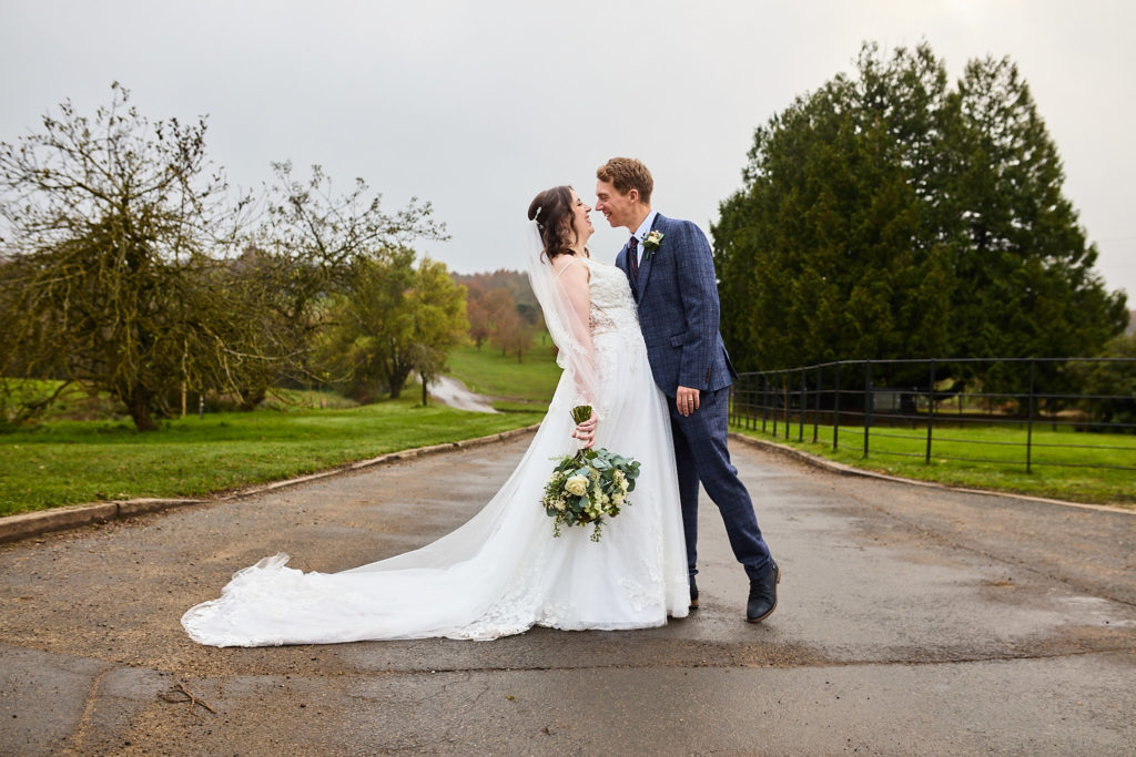 Bride and groom kissing on the tree-lined driveway at Crondon Park with the dress train spread out
