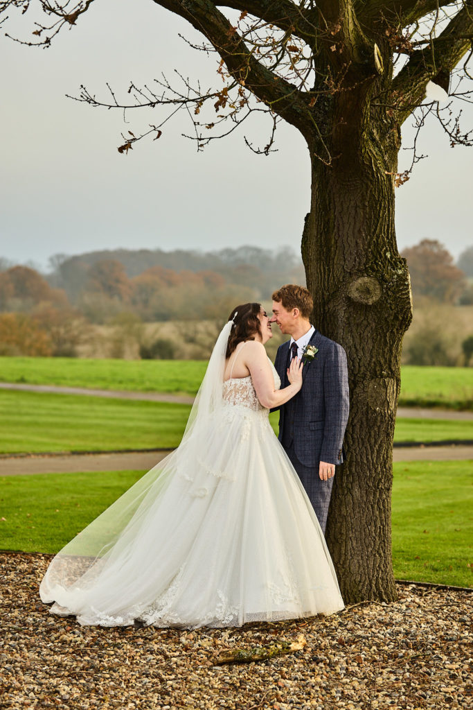 Bride and groom embracing under a bare tree with countryside behind them at Crondon Park