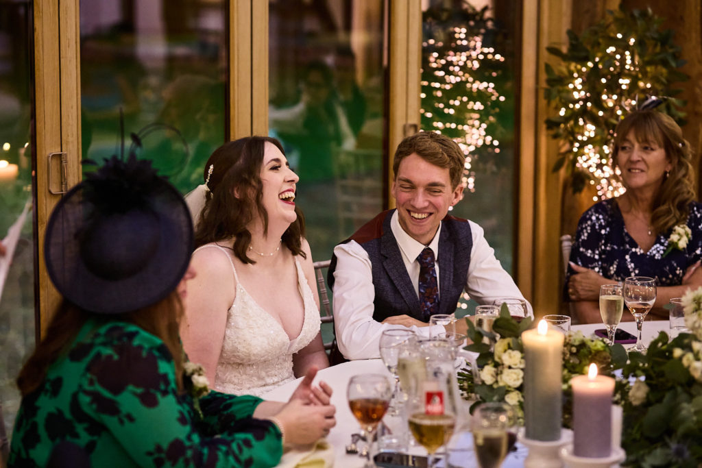 Bride and groom laughing at a candlelit table during the wedding speeches