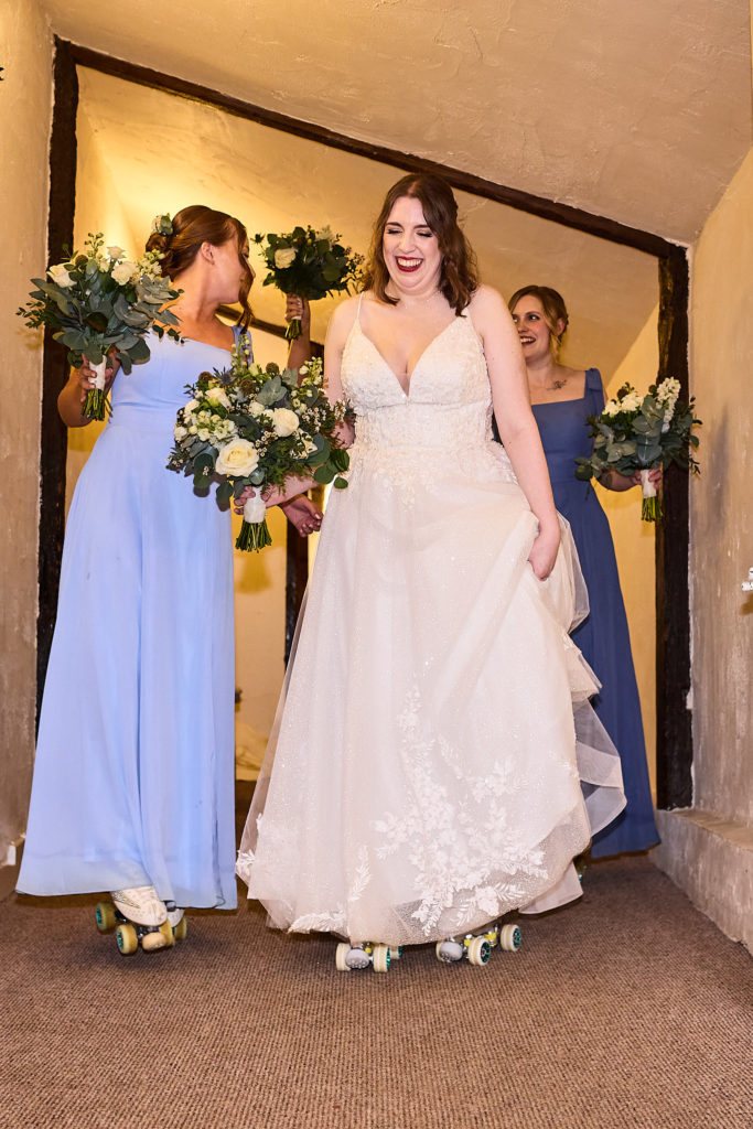 Bride on roller skates entering the barn with bridesmaids in blue dresses at Crondon Park