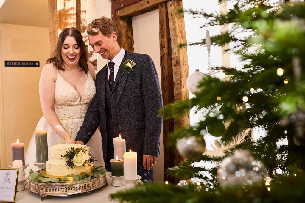 Bride and groom cutting their wedding cake beside a Christmas tree