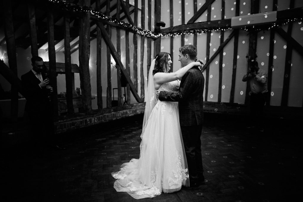 Black and white photo of the bride and groom's first dance in a timber-framed barn