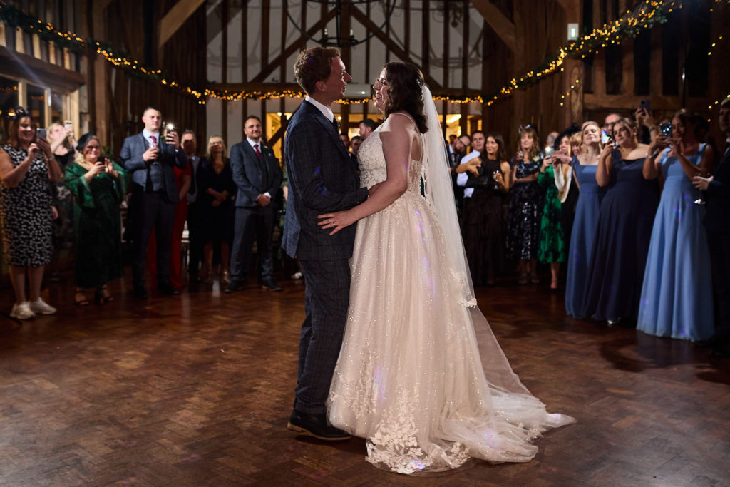 Bride and groom's first dance under fairy lights as guests watch in the barn at Crondon Park