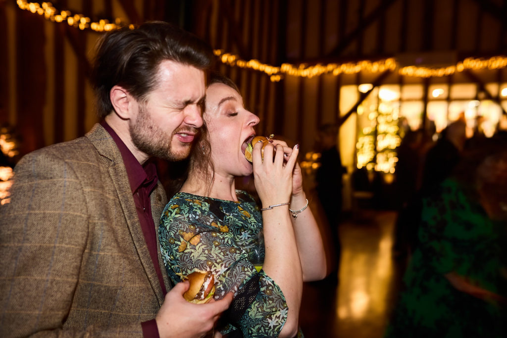 Wedding guests laughing together under fairy lights in the barn