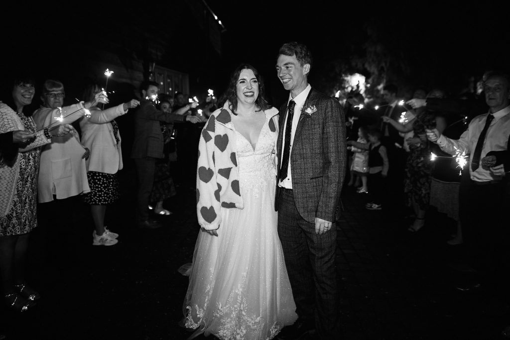 Black and white photo of the bride and groom walking between guests holding sparklers