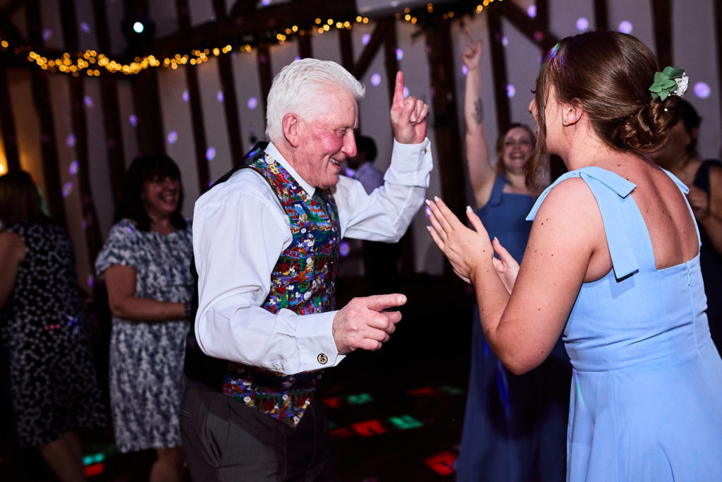 Older wedding guest in a tartan waistcoat dancing with a bridesmaid in a blue dress