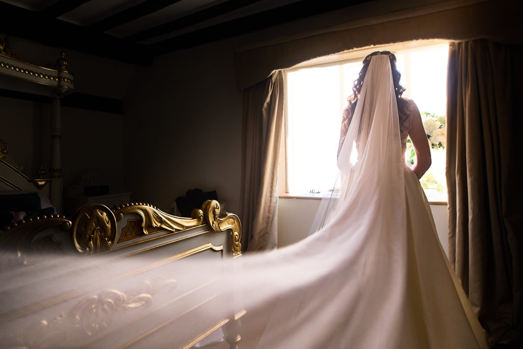 Bride standing at a window with her long veil and dress train spread across the floor