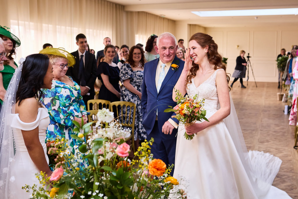Bride walking down the aisle on the arm of an older man in a navy suit