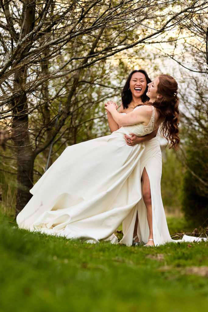 Bride lifting her wife off the ground among the trees at Prested Hall