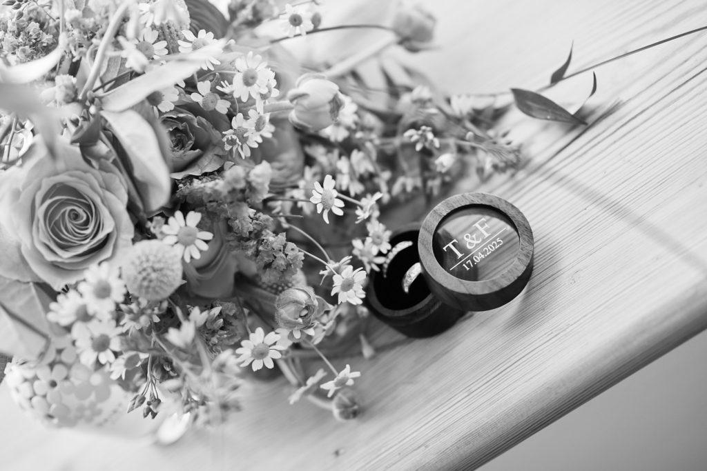 Black and white photo of wedding rings in a box beside a bouquet
