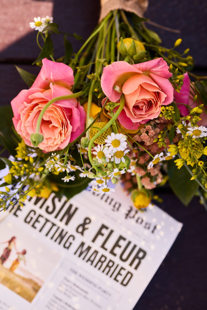 Bouquet of pink roses and wildflowers resting on the wedding newspaper