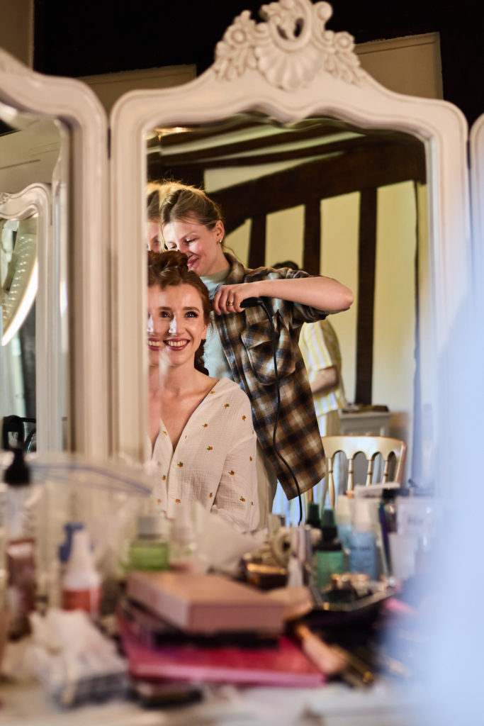 Bride having her hair styled, reflected in an ornate dressing table mirror