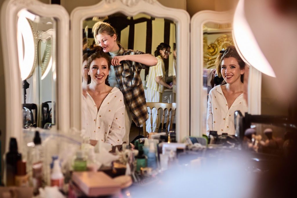 Bride smiling in a three-way mirror as her hair is styled