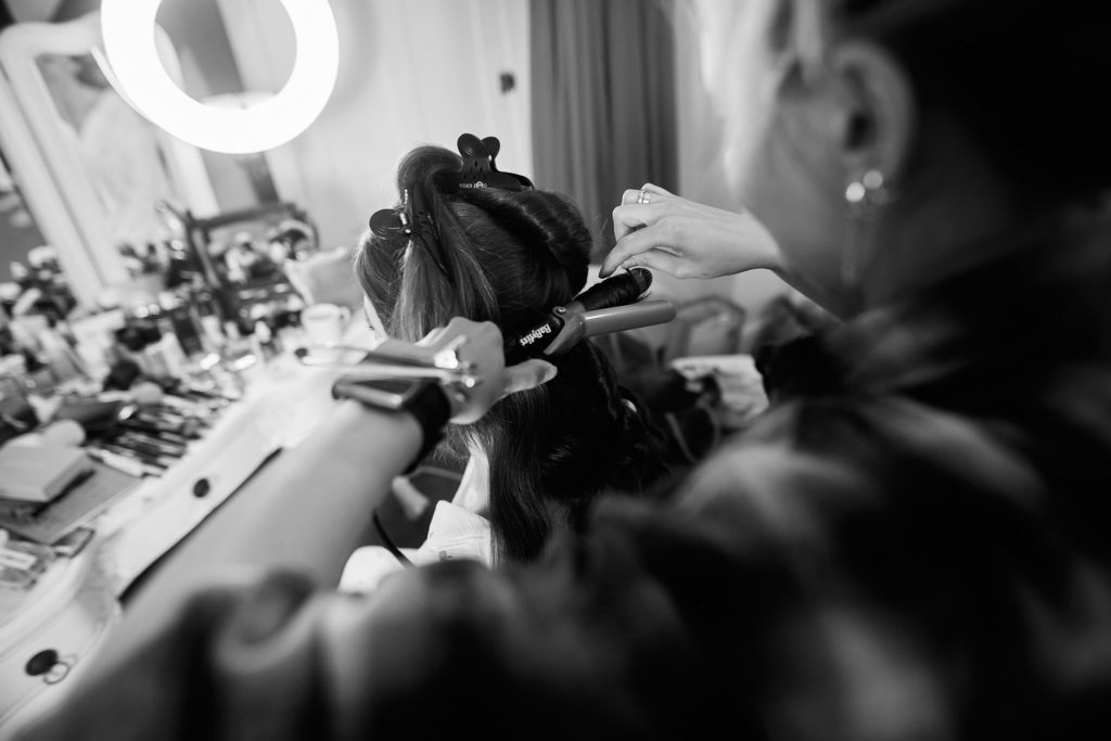 Black and white photo of a bride having her make-up applied beside a ring light
