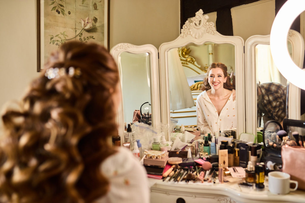 Bride with curled hair smiling into the dressing table mirror