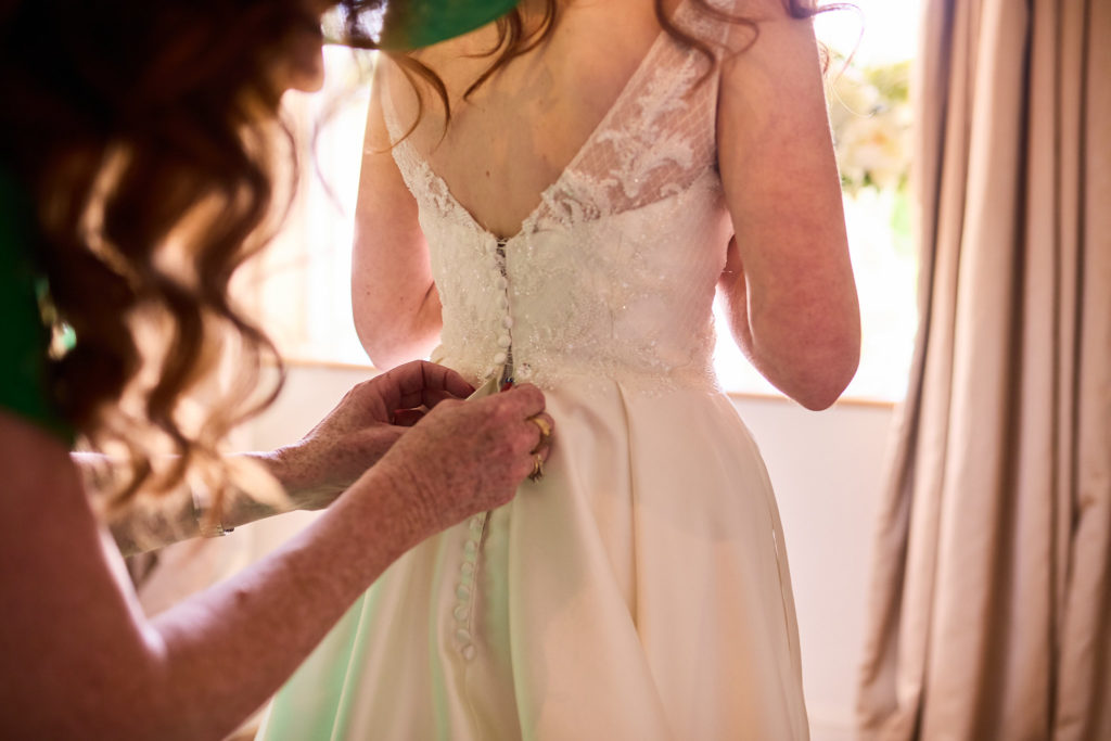 Bridesmaid fastening the buttons on the back of a bride's dress