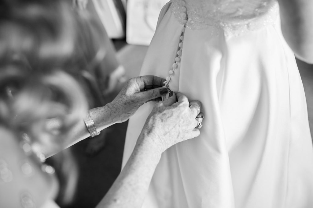 Black and white close-up of the buttons being fastened on a wedding dress