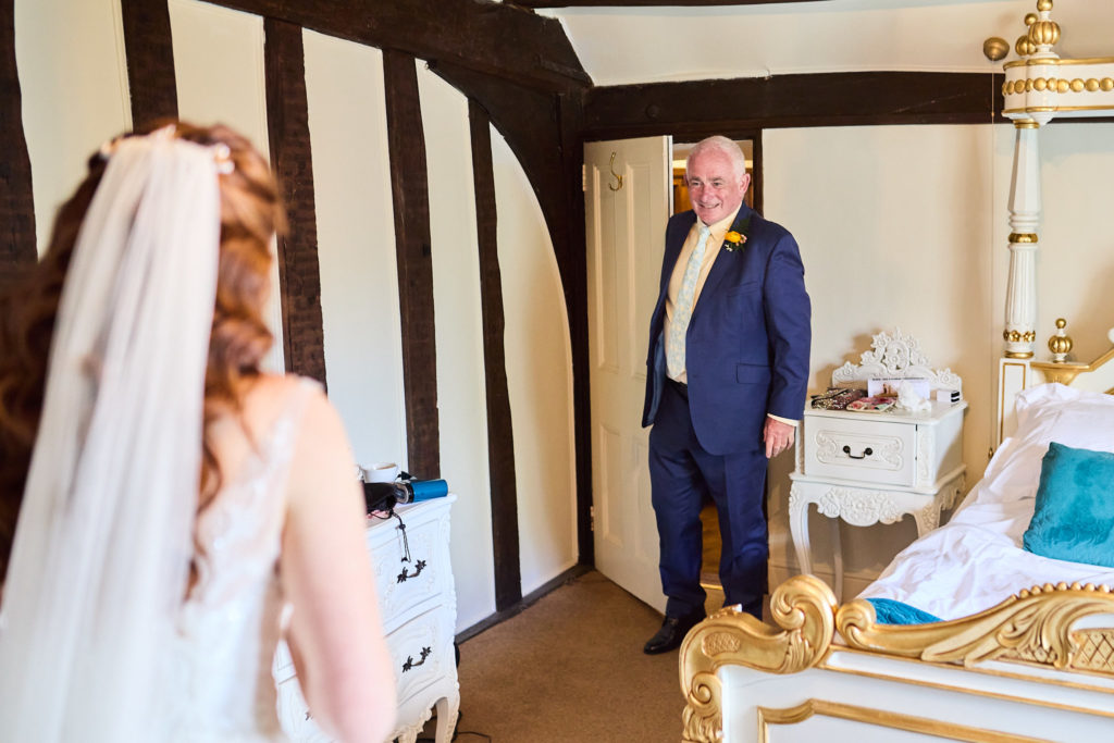 Older man in a navy suit seeing the bride in her dress for the first time