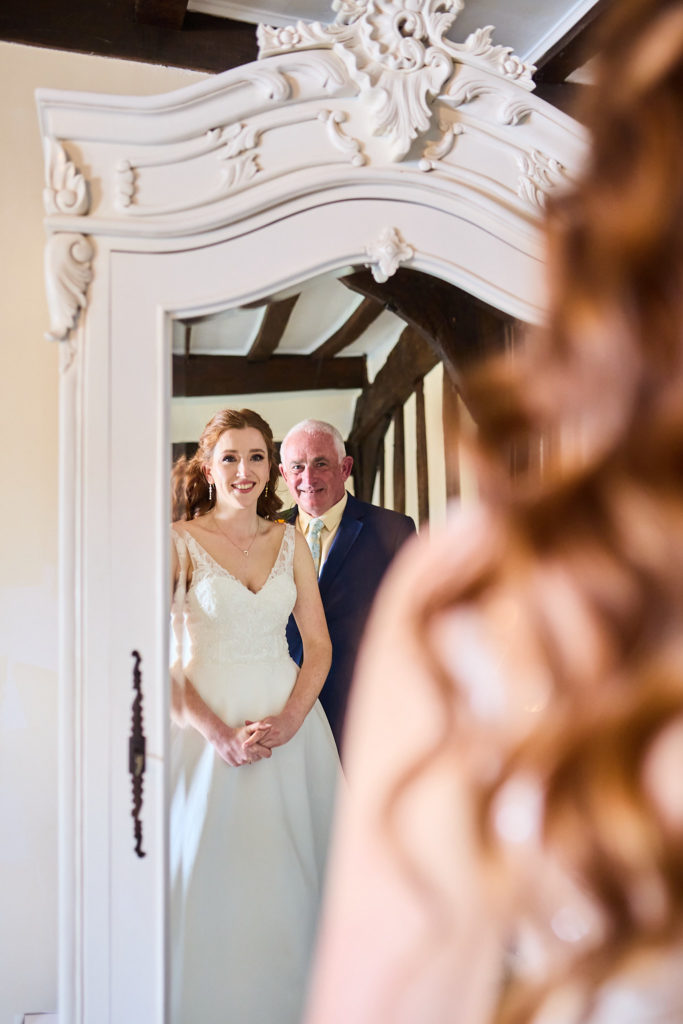 Bride and an older man in a navy suit smiling into a mirror together