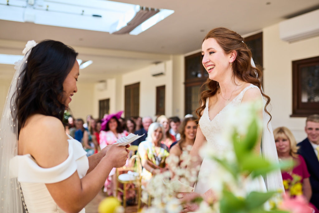 Two brides smiling at each other during their vows