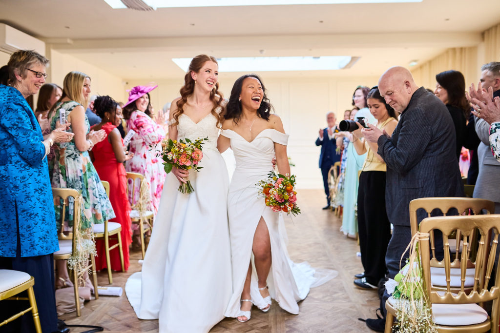 Two brides walking back down the aisle together as guests applaud
