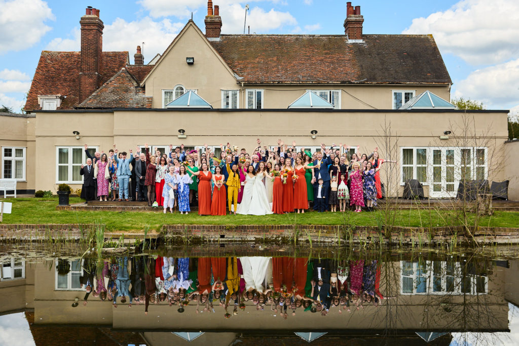 All the wedding guests lined up in front of Prested Hall, reflected in the lake