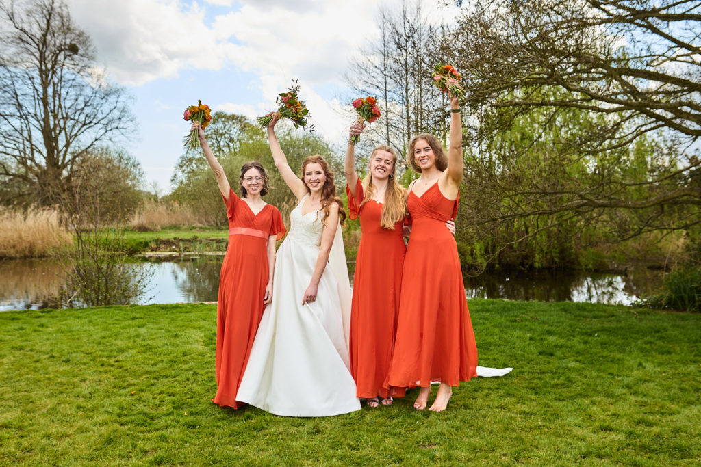 Two brides with bridesmaids in red dresses cheering with their bouquets in the air