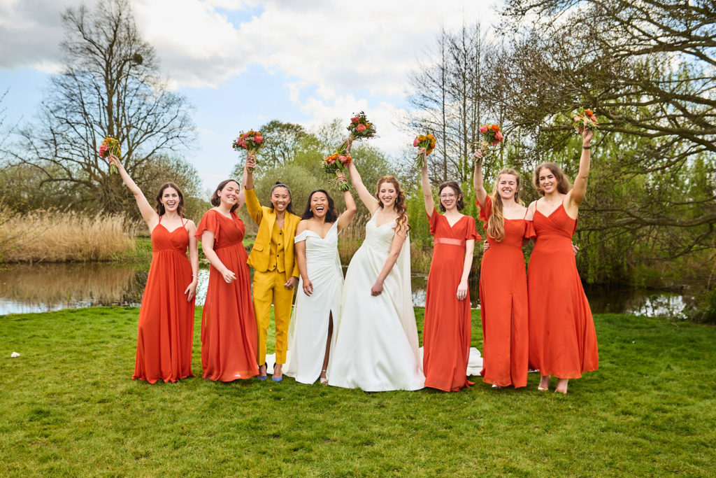 Two brides with all their bridesmaids cheering beside the lake