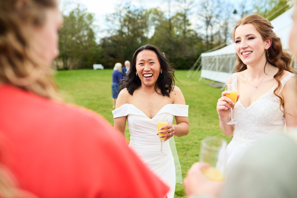 Two brides laughing with drinks at the reception