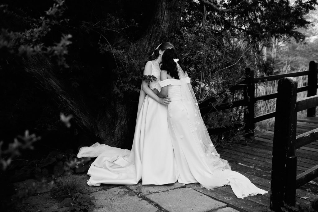 Black and white photo of the two brides embracing beside a wooden fence at Prested Hall