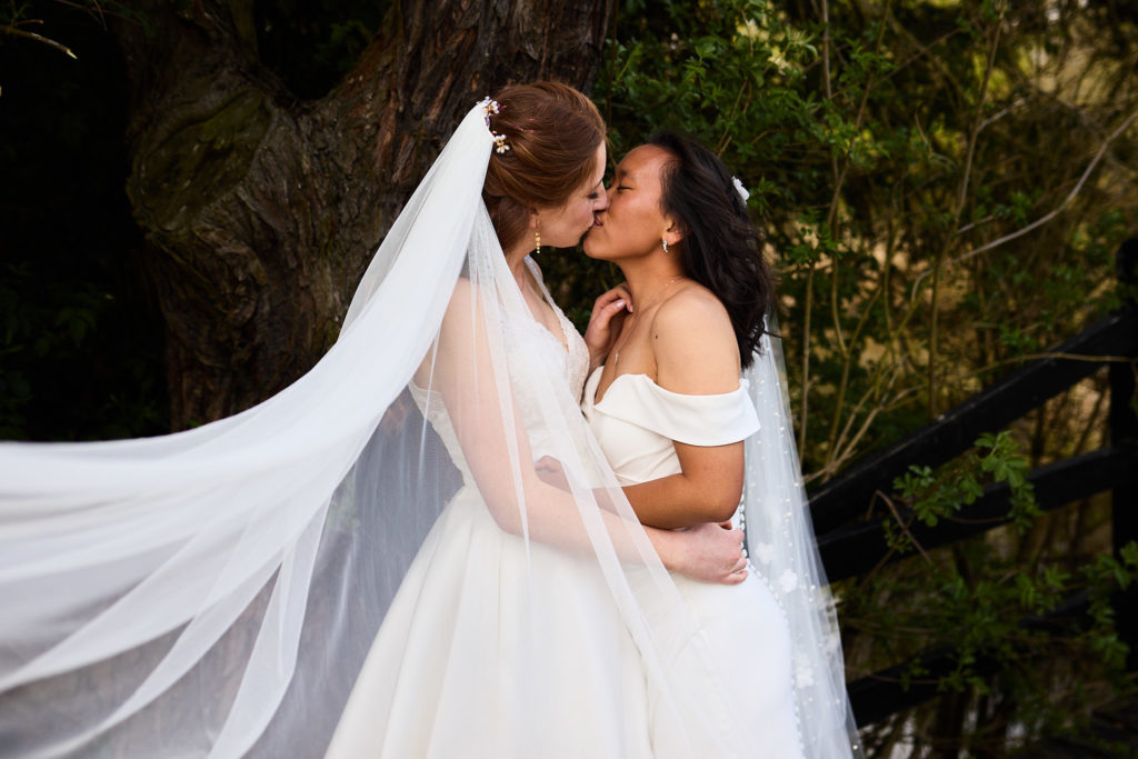 Two brides kissing with a veil sweeping round them at Prested Hall
