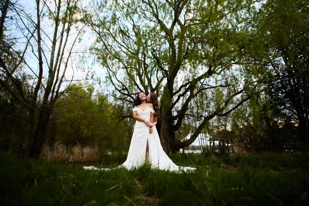 Two brides embracing beneath the trees at their LGBTQ wedding at Prested Hall, Essex
