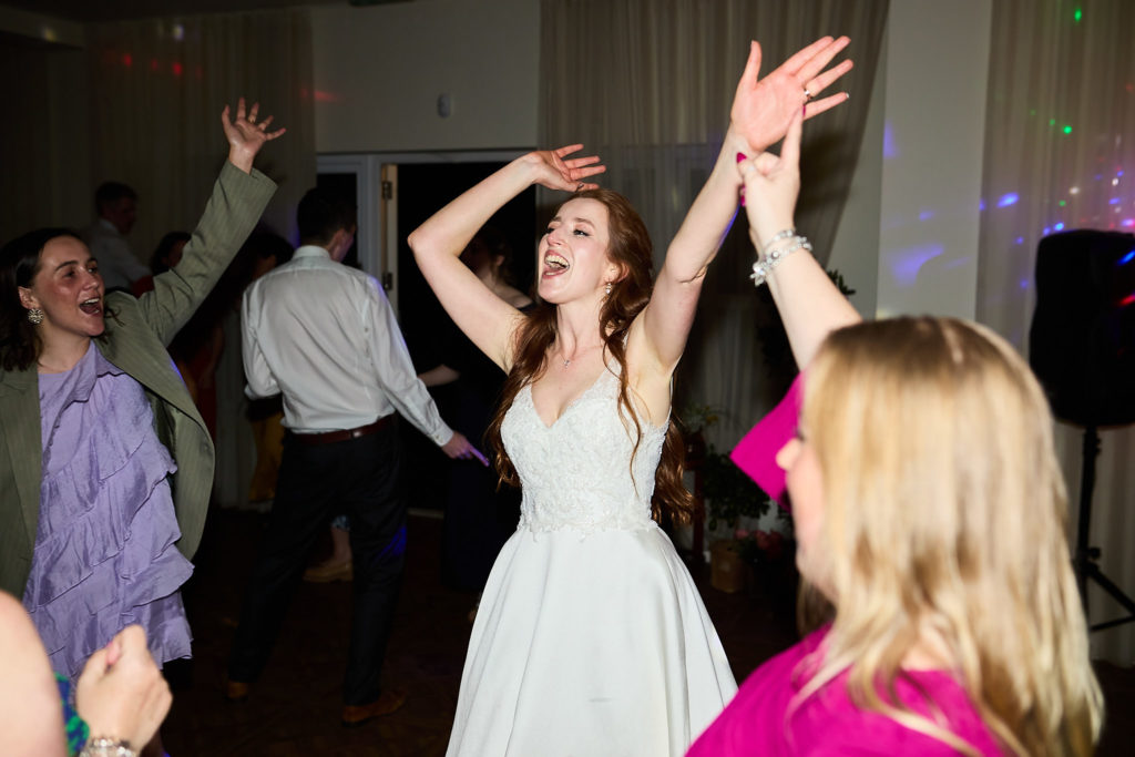 Bride dancing with her arms in the air among guests