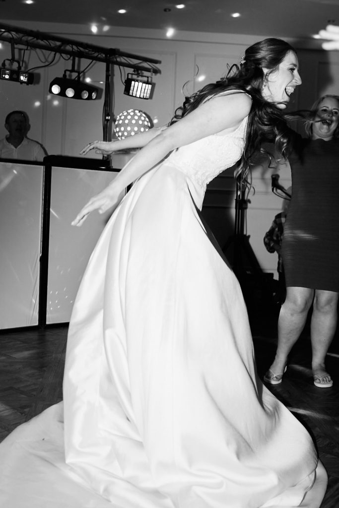 Black and white photo of a bride swirling her dress on the dance floor