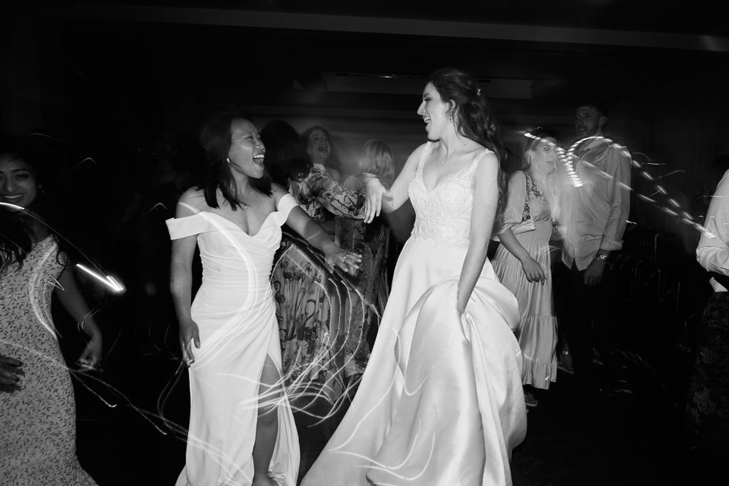 Black and white photo of the two brides dancing among their guests