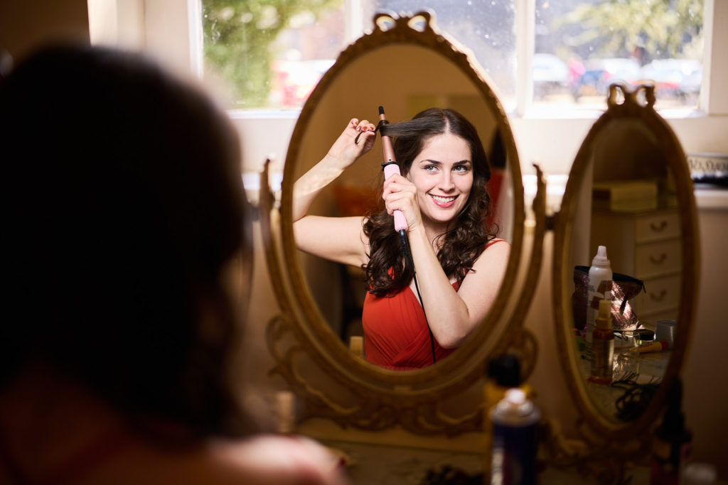 Bridesmaid in a red dress fixing her hair in a mirror